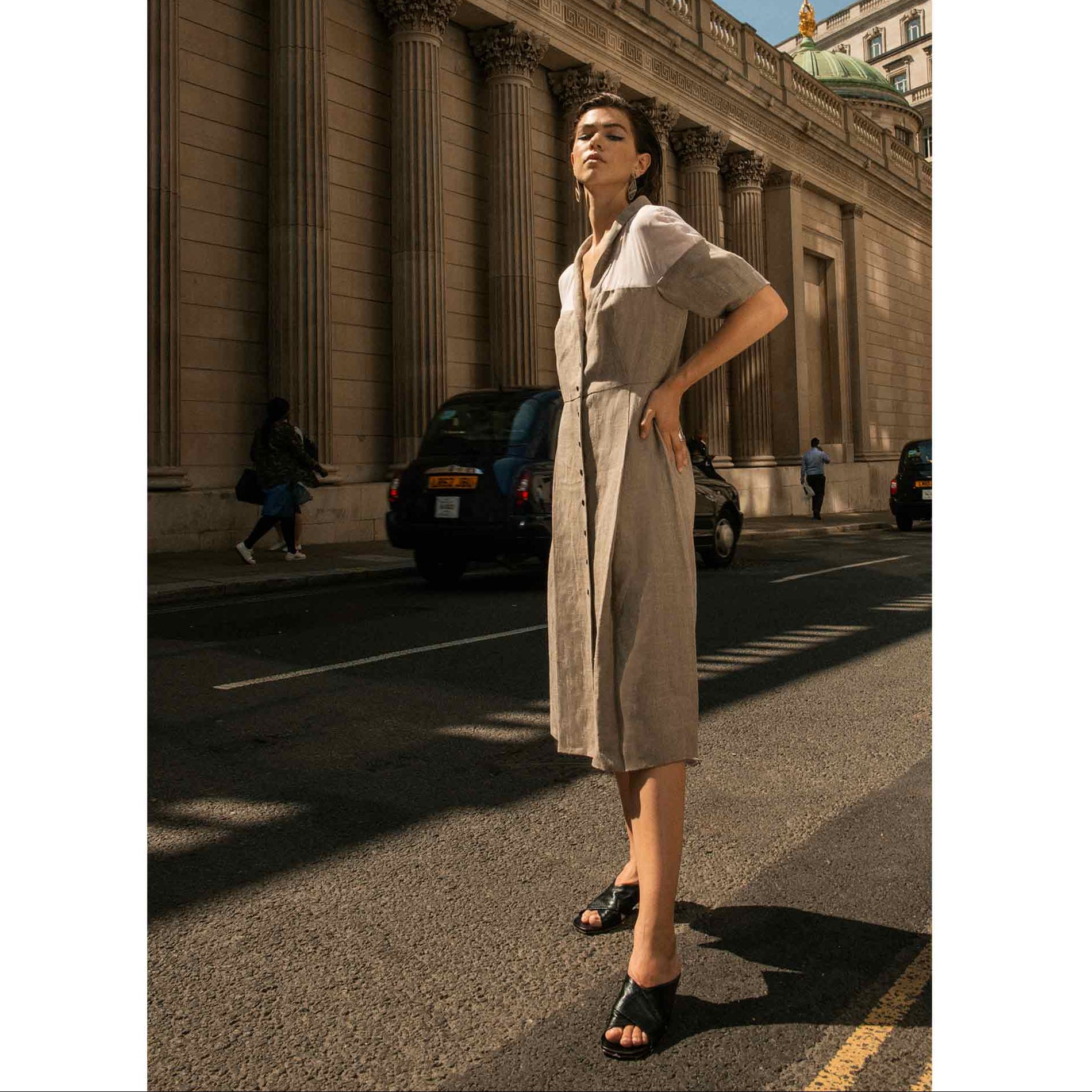Women’s clean black leather slide heels with open toe being worn by a woman in a casual tan dress
