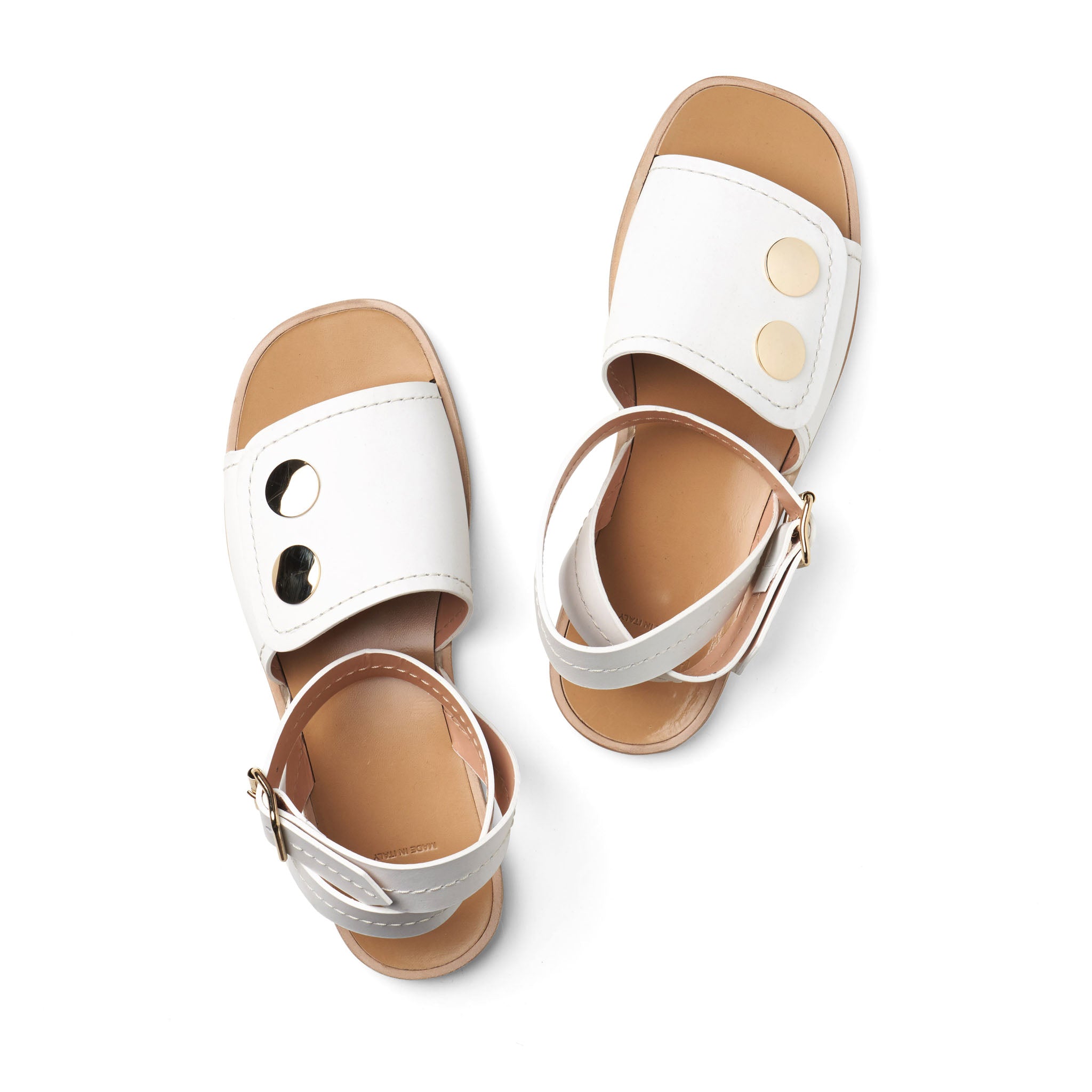 pair of white sandals for women shown has softly squared off toe shape, open toe with crossover strap at ankle, oversized gold metal studs and buckle detail 