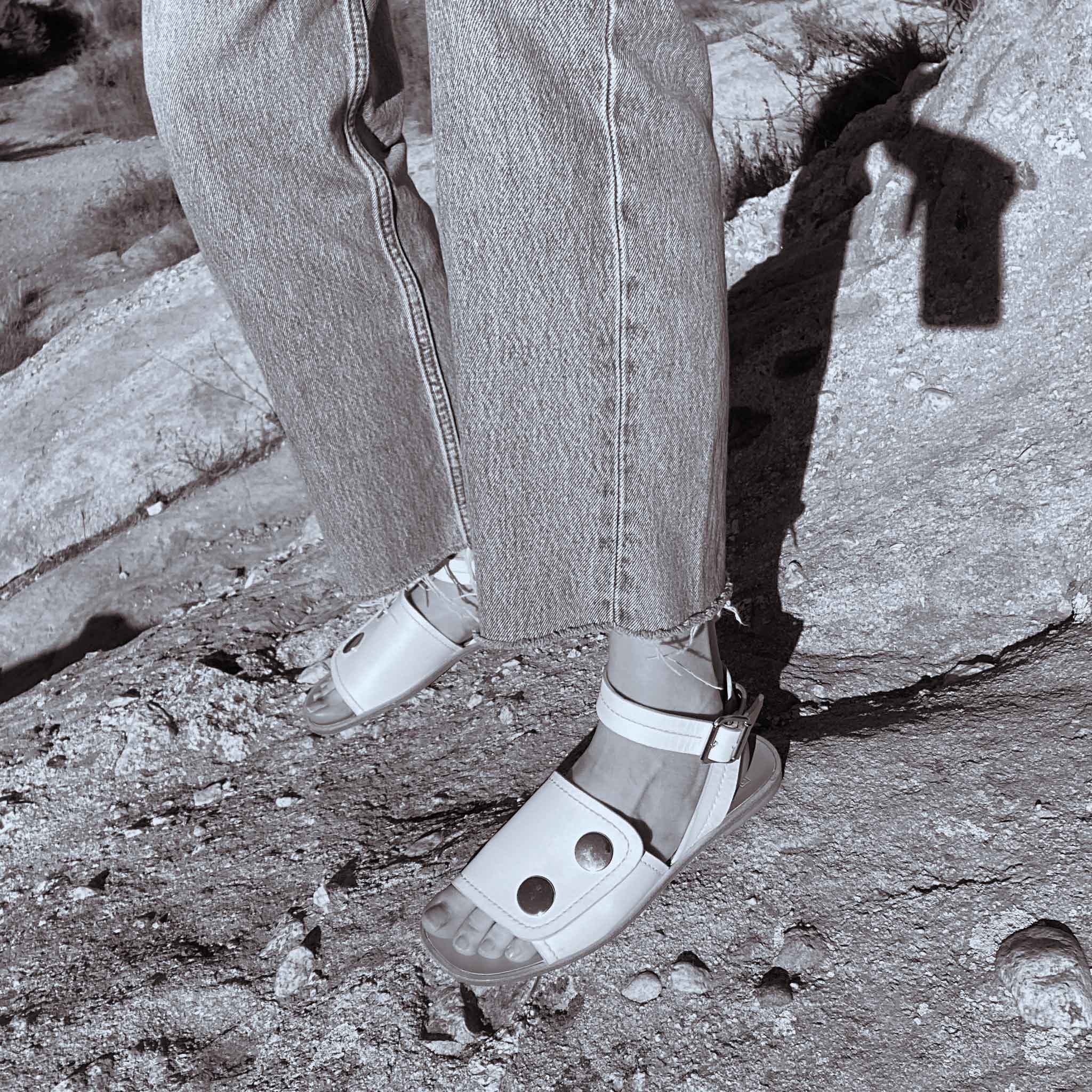 black and white photo of raw edge Levis denim and casual white leather ankle strap sandals